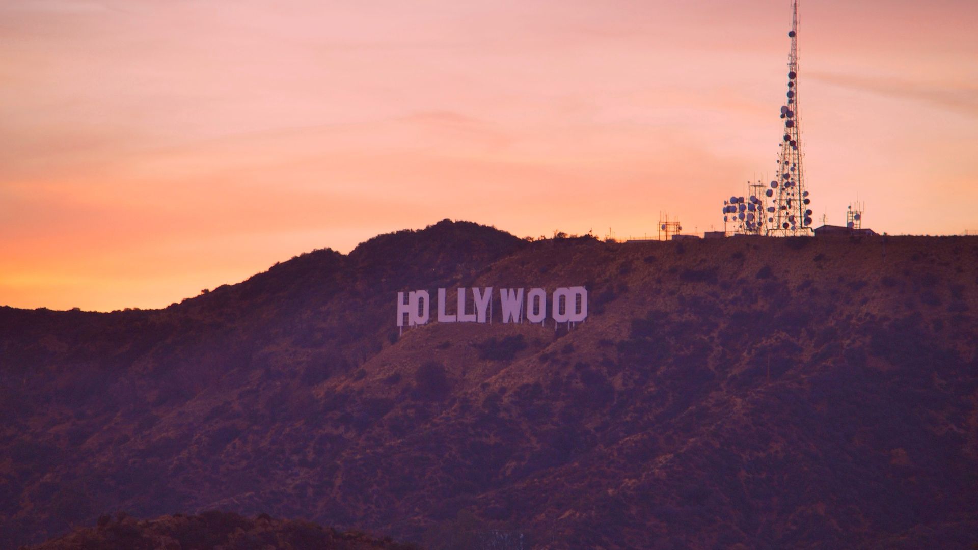 The image features the iconic Hollywood sign on a hill with a radio antenna nearby, set against a beautiful sunset sky.