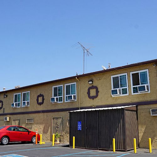 This image shows a motel, with the sign reading “Holly Crest Hotel,” a predominantly brown exterior, and a red car parked in front of it.