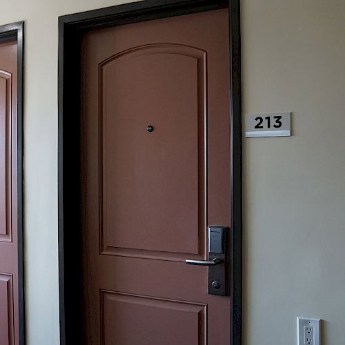 The image shows two brown doors in a hallway; the door on the right is labeled with the number 