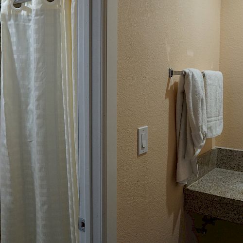 The image depicts a bathroom with a sink, a granite countertop, a wall mirror, and a towel on a rack. There is a shower with a curtain to the left.