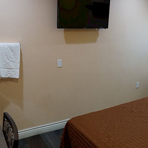 A small hotel room with a bed, wall-mounted TV, sink, towel, and curtains covering a window is shown.