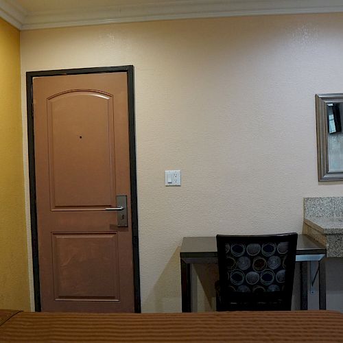 A small room with a bed, desk, chair, sink, mirror, towel, closed door, and yellow and beige walls.