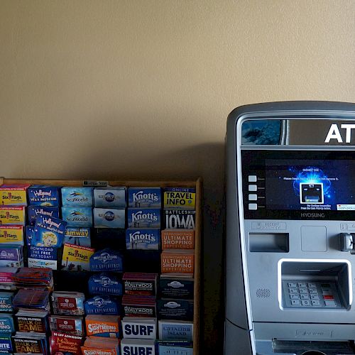 An ATM machine is positioned next to a rack filled with various pamphlets and brochures against a beige wall.