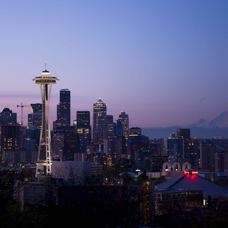 The image shows the Seattle skyline at dusk, featuring the Space Needle and various skyscrapers with Mount Rainier visible in the background.