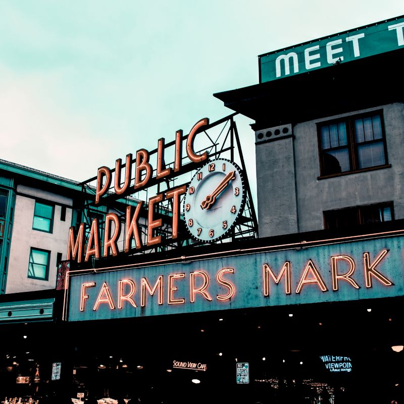 The image shows an urban scene with neon signs indicating "Public Market" and "Farmers Market", likely representing a well-known market.