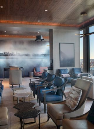 A modern lounge with multiple seating areas, large windows with a coastal view, and a mural on the back wall depicting a city skyline.