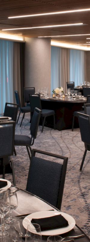 A well-lit banquet hall with round tables set for a formal event, featuring dark chairs, elegant place settings, and floral centerpieces.