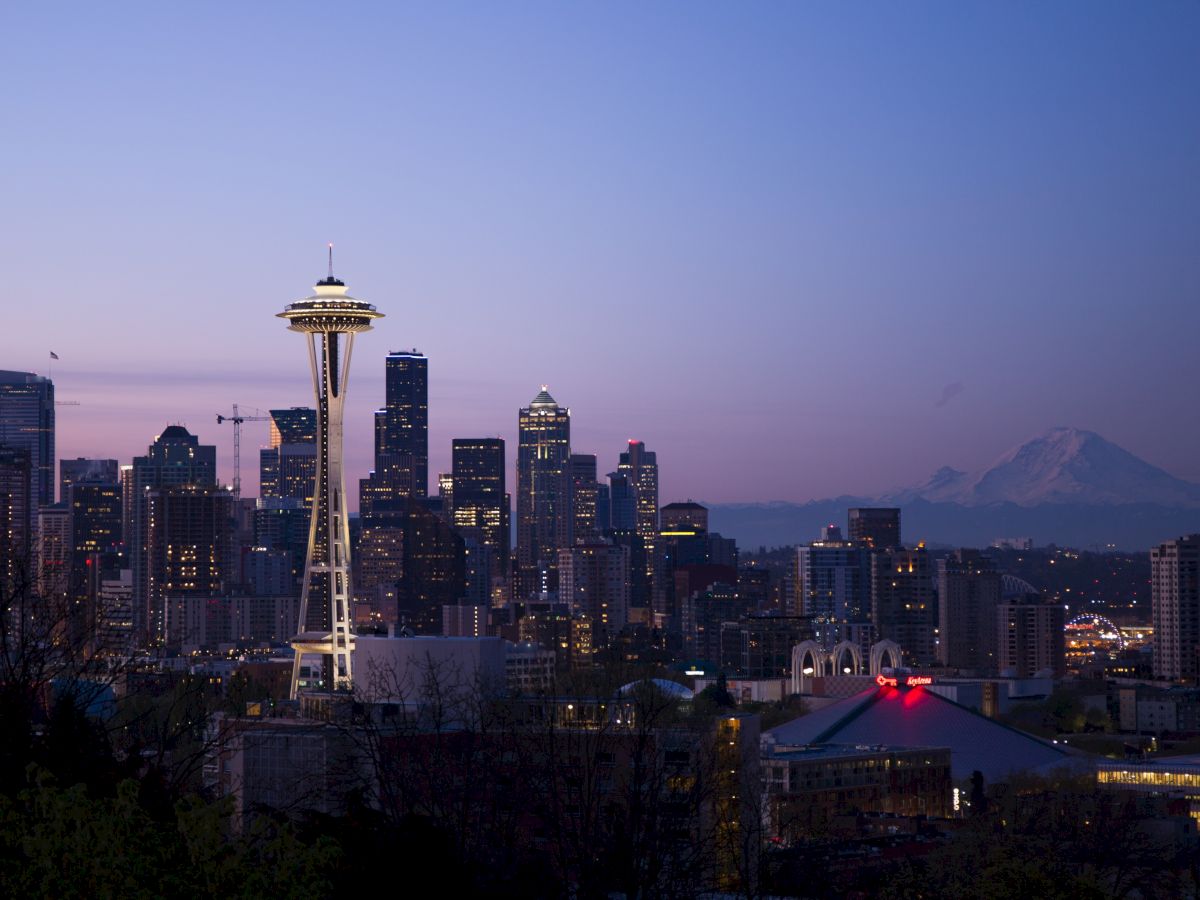 The image depicts the Seattle skyline at dusk, featuring the Space Needle prominently, with Mount Rainier visible in the background.