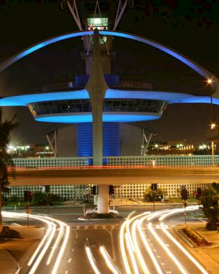 A night view of the illuminated Theme Building at Los Angeles International Airport (LAX) with light streaks from passing cars and nearby parking structures.